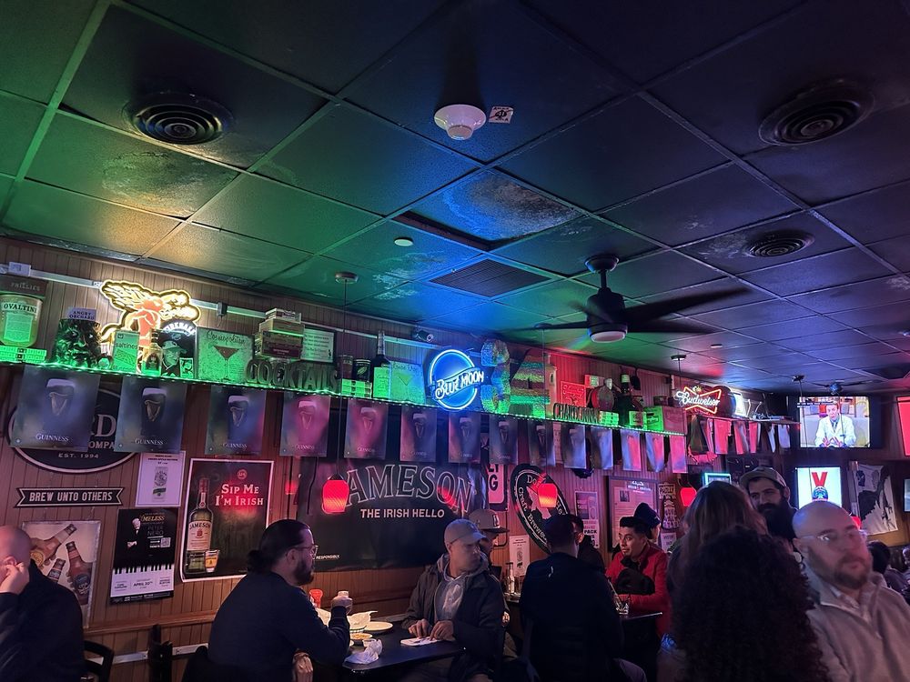 Wood-paneled interior of Locust Rendezvous with neon beer signs lining the wall and patrons seated at tables.